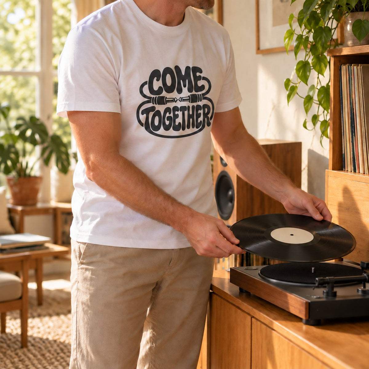 Man in a white Come Together tee putting a record on a turntable at home