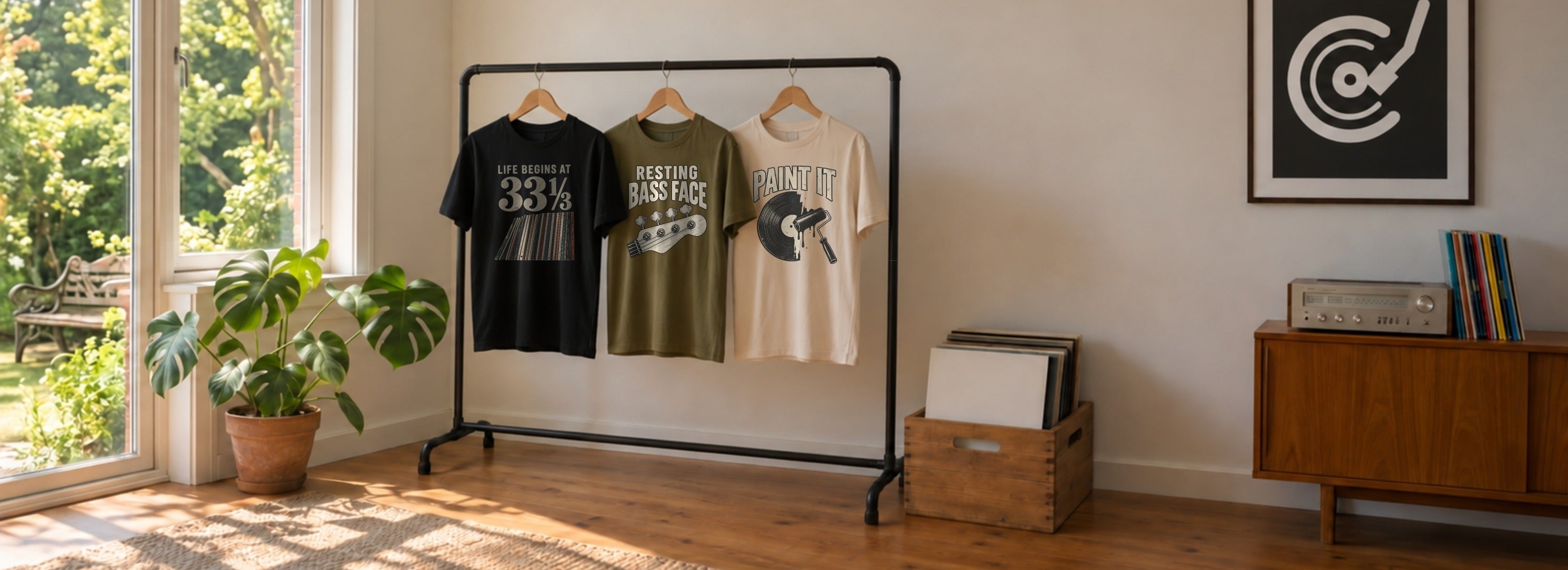 NeedleDrop Tees - rack of three graphic tees in a warm living room, with a monstera plant, a window, a record crate, and a vintage tuner